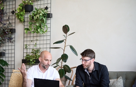 Deux hommes en discussion professionnelle devant un ordinateur portable dans un bureau avec plantes