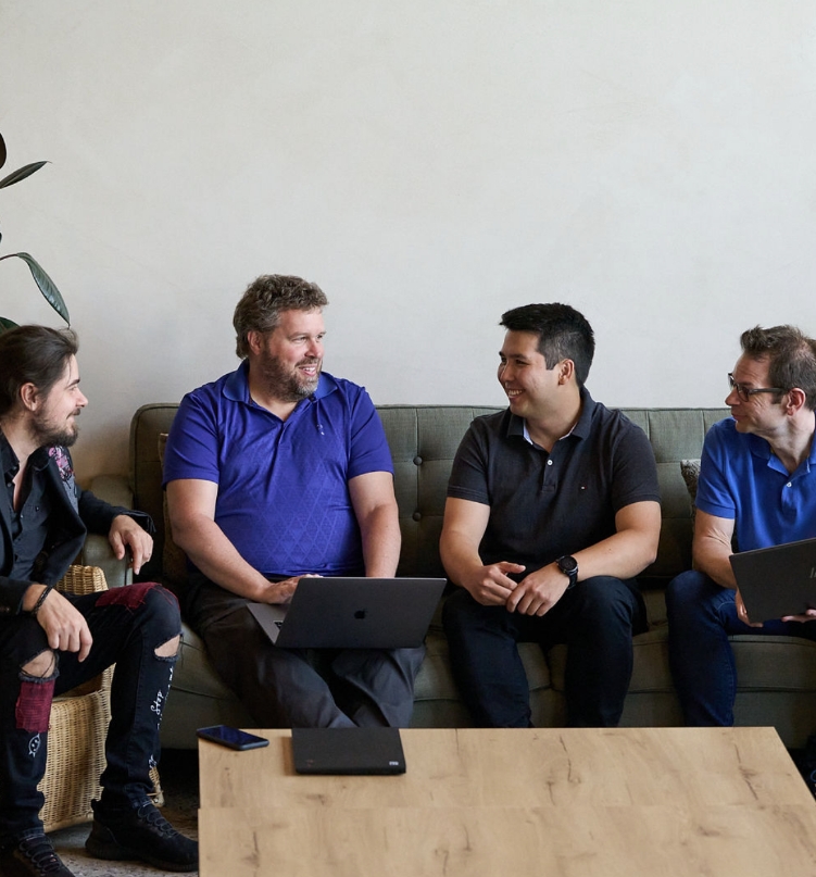 Quatre hommes en discussion informelle assis sur un canapé avec ordinateurs portables