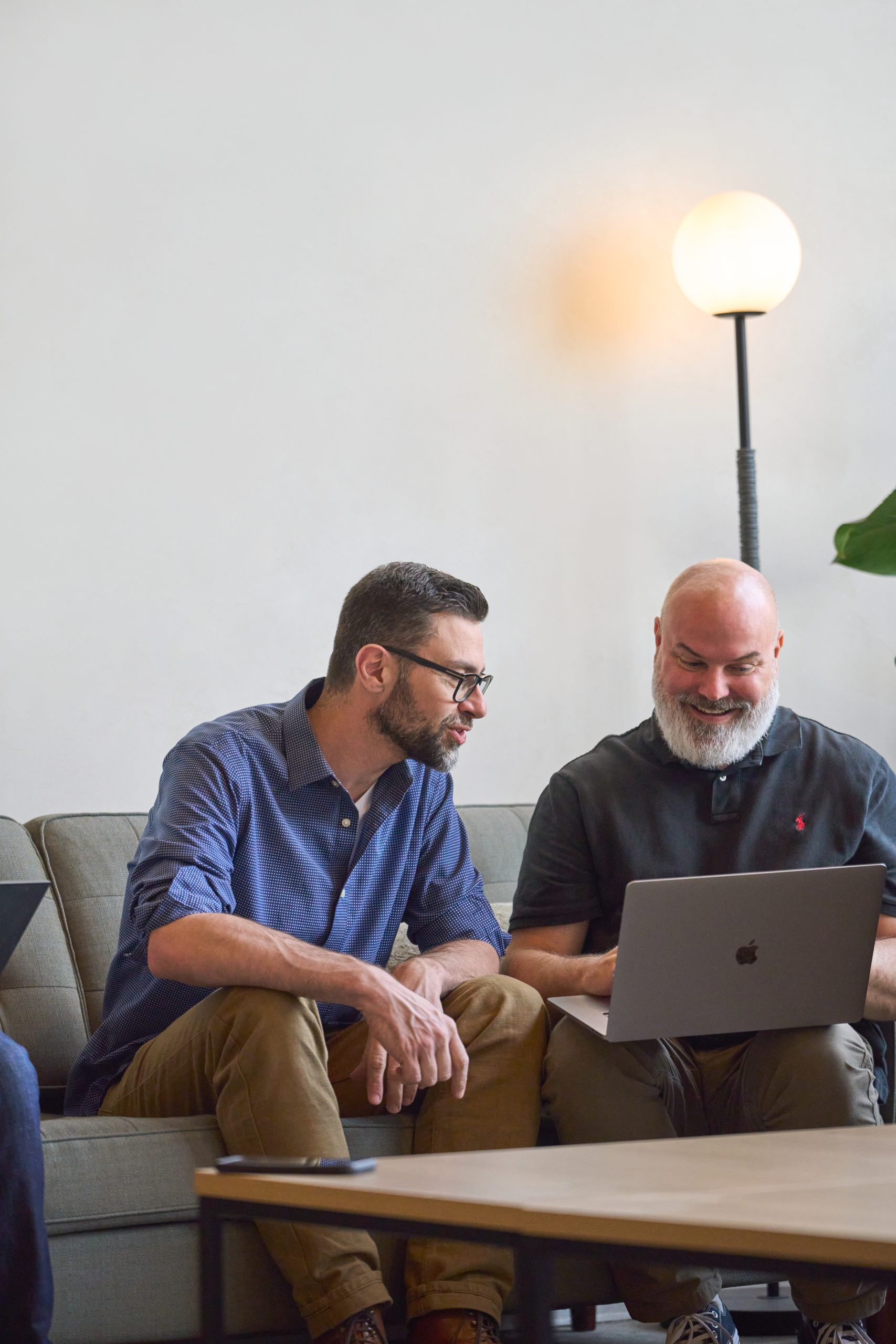Discussion entre un professionnel et un client assis sur un canapé, échangeant autour d’un ordinateur portable